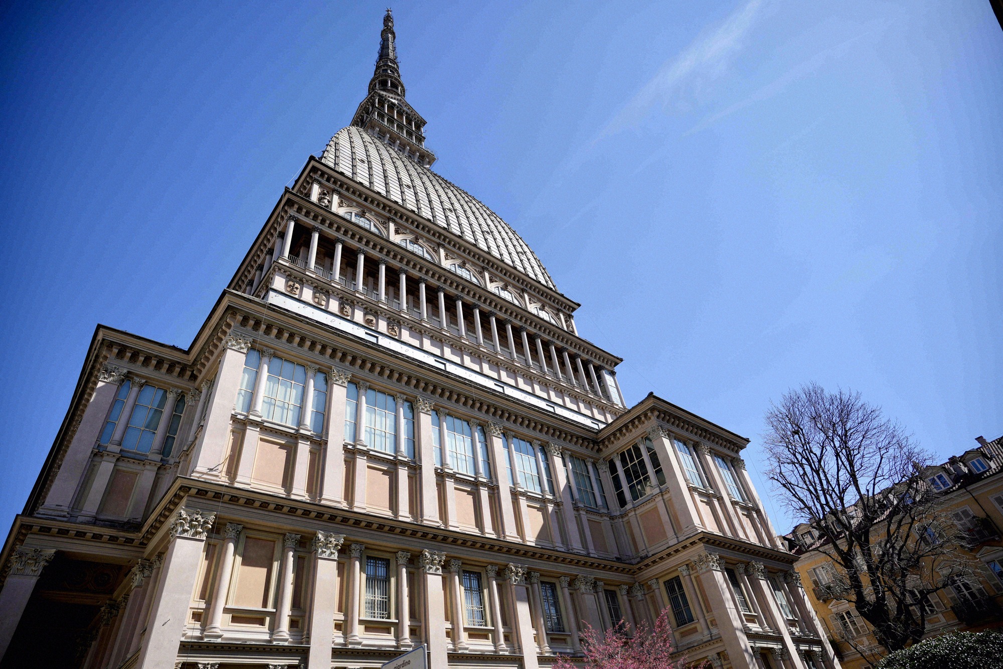 Nahaufnahme der Mole Antonelliana von unten mit Blick auf die charakteristische Kuppel und die gestufte Turmspitze vor blauem Himmel.