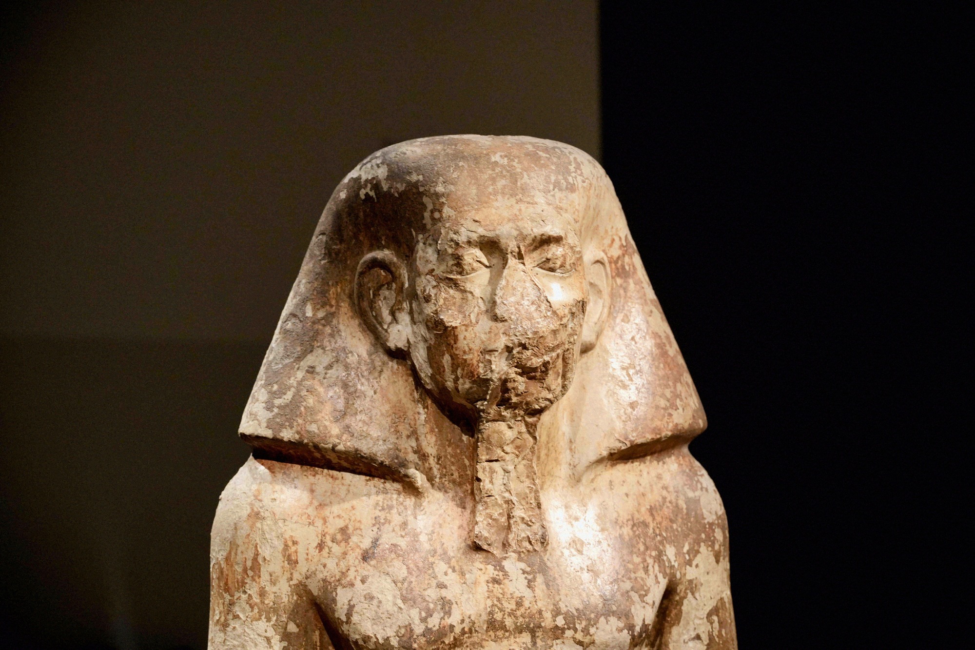 Nahaufnahme einer altägyptischen Pharaonenstatue aus Granit im Museo Egizio di Torino vor dunklem Ausstellungshintergrund.
